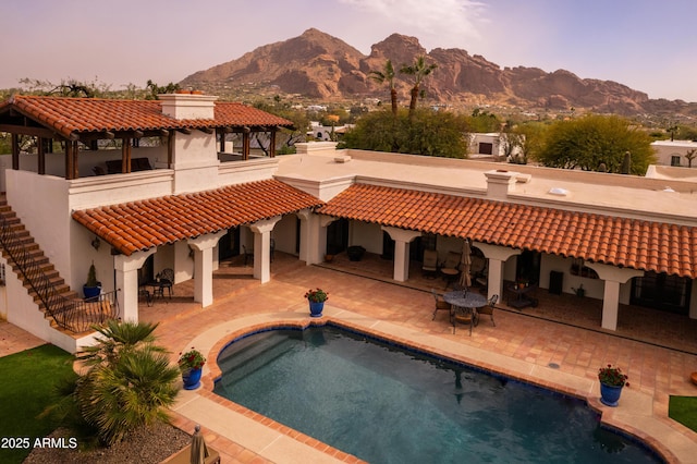 back of property at dusk with a patio area, a chimney, a mountain view, and a tiled roof