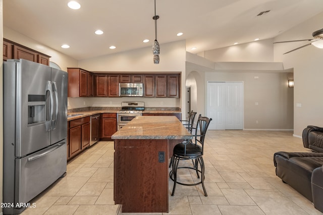 kitchen with light stone counters, appliances with stainless steel finishes, ceiling fan, a kitchen bar, and hanging light fixtures