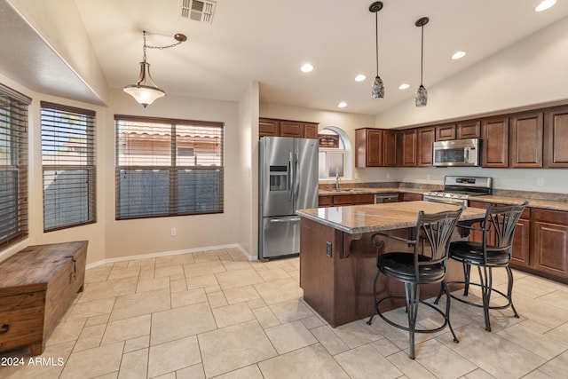 kitchen with decorative light fixtures, vaulted ceiling, stainless steel appliances, a kitchen breakfast bar, and a center island