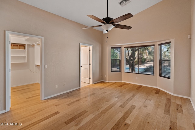 unfurnished bedroom with high vaulted ceiling, a closet, light hardwood / wood-style floors, ceiling fan, and a walk in closet