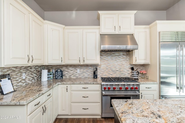 kitchen with backsplash, dark hardwood / wood-style flooring, light stone countertops, wall chimney exhaust hood, and premium appliances
