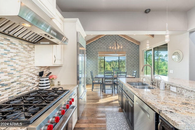 kitchen featuring wall chimney range hood, high quality appliances, hanging light fixtures, sink, and white cabinets