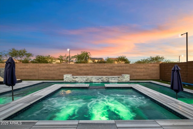 pool at dusk featuring an in ground hot tub