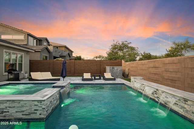 pool at dusk with an in ground hot tub, pool water feature, a grill, and a patio