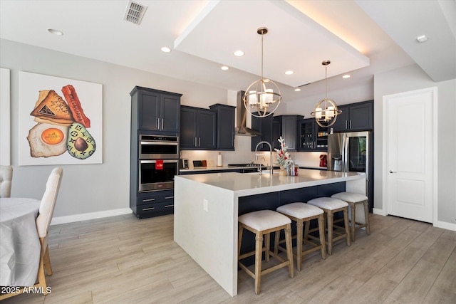 kitchen featuring decorative light fixtures, a kitchen breakfast bar, wall chimney exhaust hood, a center island with sink, and light hardwood / wood-style flooring