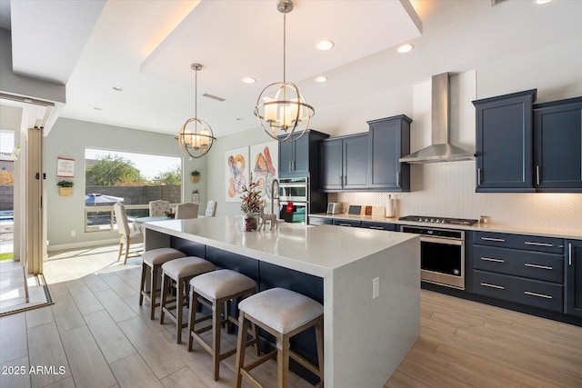 kitchen with wall chimney exhaust hood, a breakfast bar area, hanging light fixtures, and a center island with sink