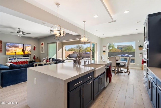 kitchen featuring oven, hanging light fixtures, a center island with sink, and light hardwood / wood-style flooring