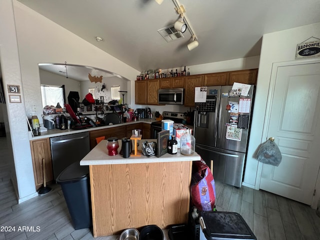 kitchen with appliances with stainless steel finishes, kitchen peninsula, light hardwood / wood-style flooring, and track lighting