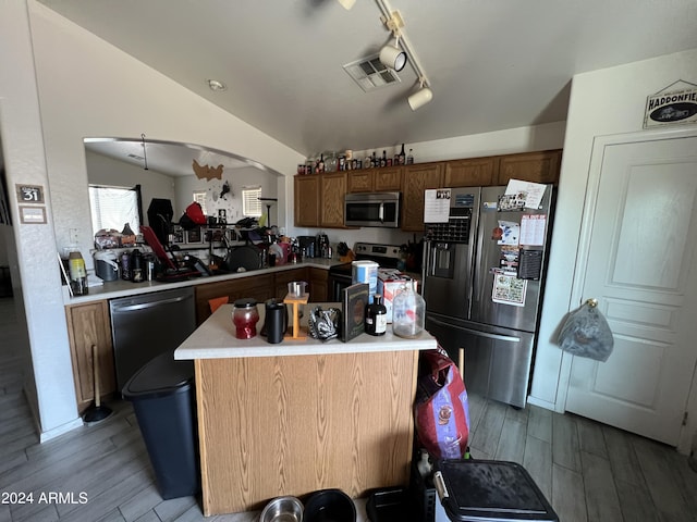 kitchen featuring a kitchen island, light countertops, vaulted ceiling, appliances with stainless steel finishes, and light wood-type flooring