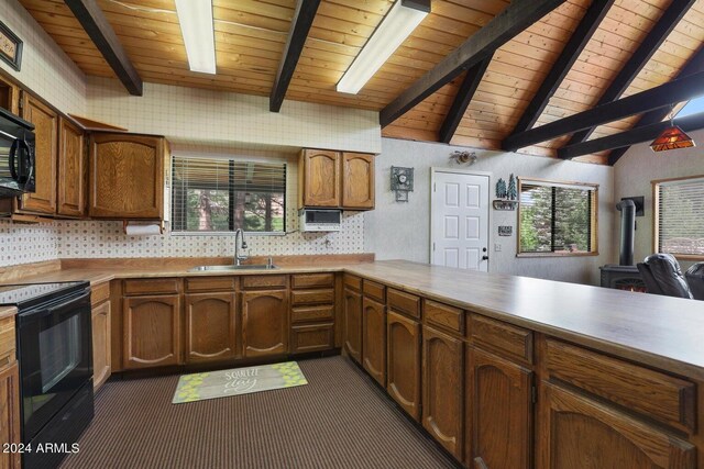 kitchen featuring a wealth of natural light, a wood stove, black appliances, a sink, and vaulted ceiling with beams