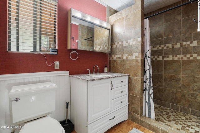 bathroom with a tile shower, wainscoting, vanity, and toilet