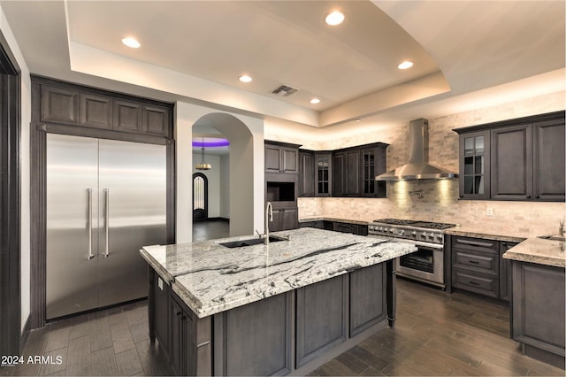 7254 E Sonoran Trl, Scottsdale, AZ 85266 - kitchen featuring premium appliances, a tray ceiling, wall chimney exhaust hood, arched walkways, and dark wood-style flooring