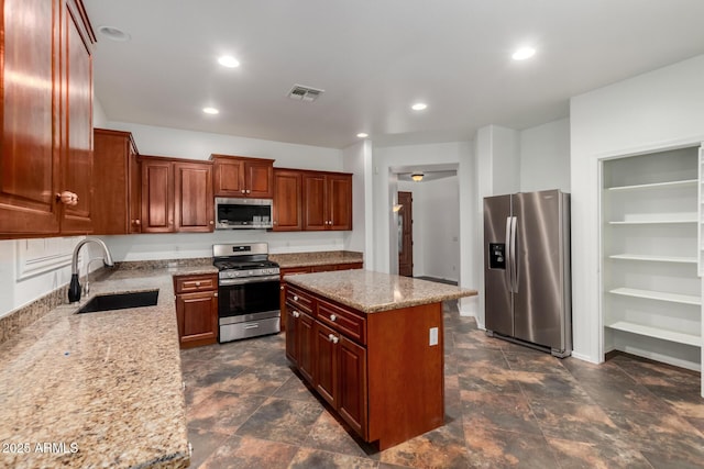 kitchen featuring light stone countertops, stainless steel appliances, a kitchen island, and sink