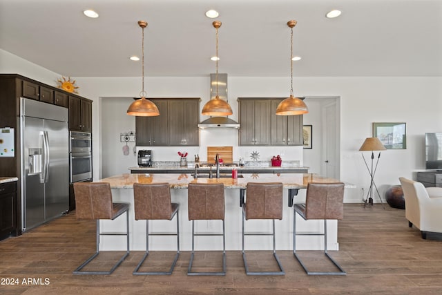 kitchen featuring a kitchen island with sink, light stone countertops, wall chimney range hood, and appliances with stainless steel finishes