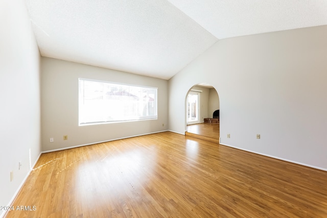 unfurnished room with a textured ceiling, vaulted ceiling, and hardwood / wood-style flooring