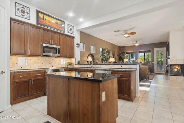 kitchen featuring light tile patterned flooring, decorative backsplash, appliances with stainless steel finishes, a kitchen island, and kitchen peninsula