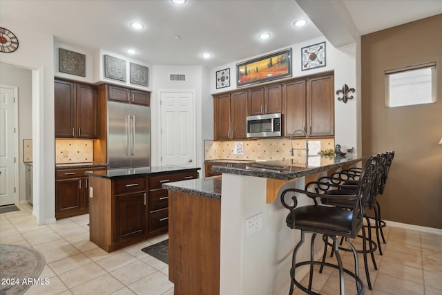 kitchen with a breakfast bar, a center island, stainless steel appliances, and dark stone counters