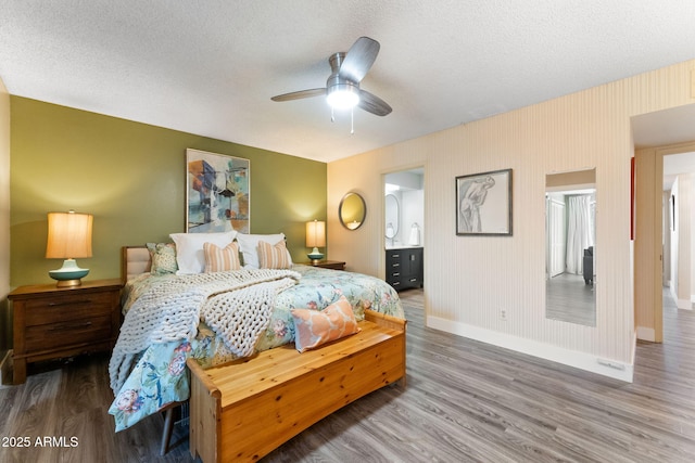 bedroom with wood finished floors, baseboards, ensuite bathroom, and a textured ceiling