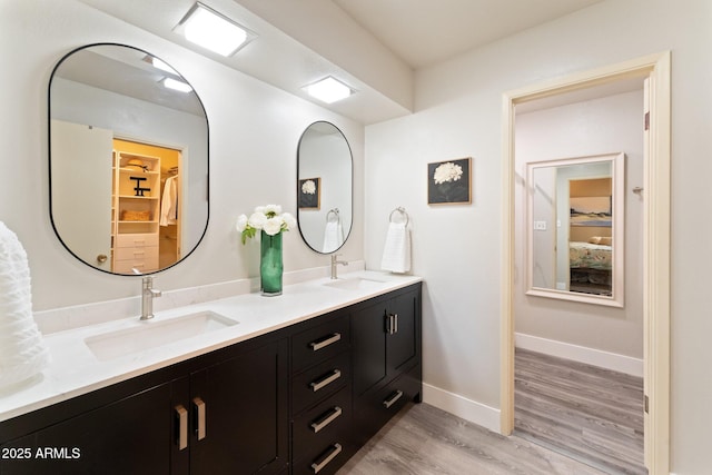 full bath with double vanity, wood finished floors, baseboards, and a sink