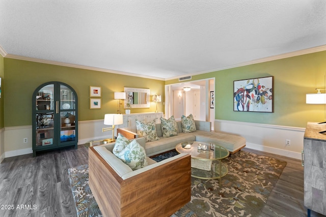 living area with wood finished floors, a wainscoted wall, visible vents, ornamental molding, and a textured ceiling