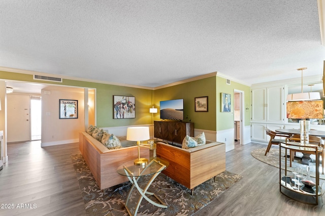 living room featuring visible vents, ornamental molding, a textured ceiling, and wood finished floors