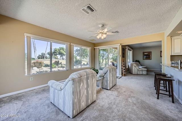 living room featuring ceiling fan, light colored carpet, and a textured ceiling