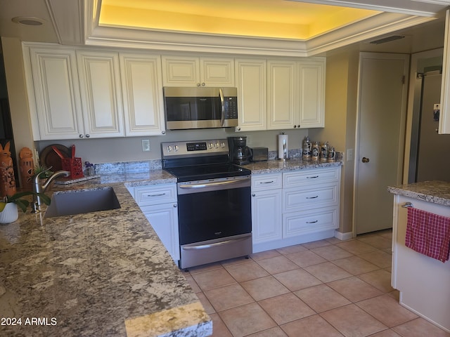 kitchen with light stone counters, stainless steel appliances, a tray ceiling, sink, and light tile patterned floors