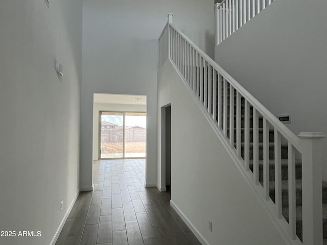 stairs featuring a towering ceiling, wood tiled floor, and baseboards