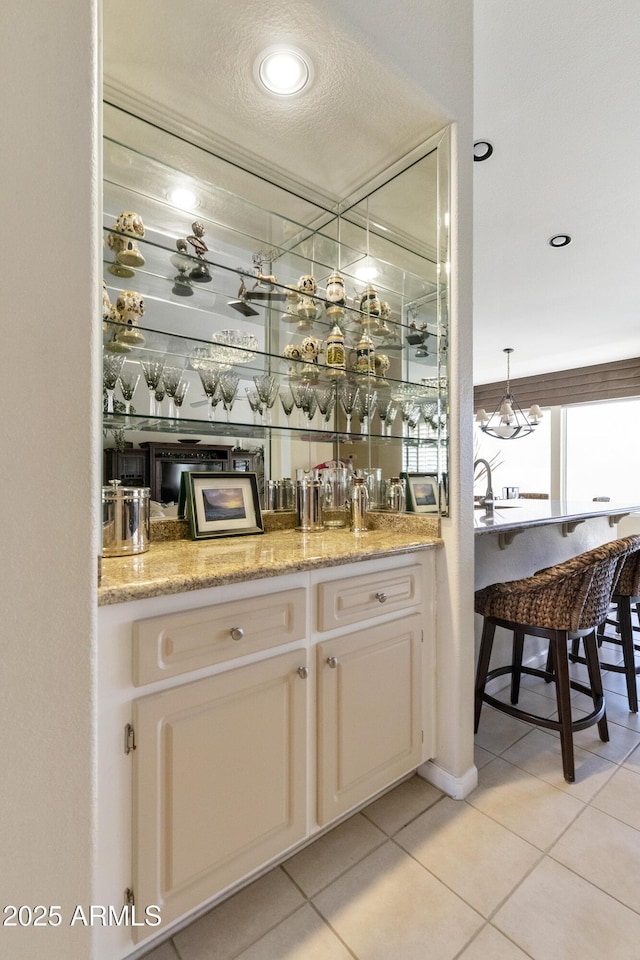 bar featuring a textured ceiling, white cabinetry, light tile patterned flooring, light stone countertops, and pendant lighting