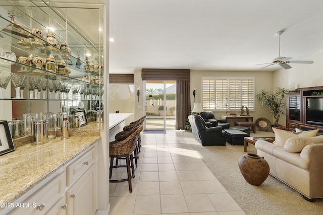 bar with light stone countertops, light tile patterned flooring, ceiling fan, and white cabinetry