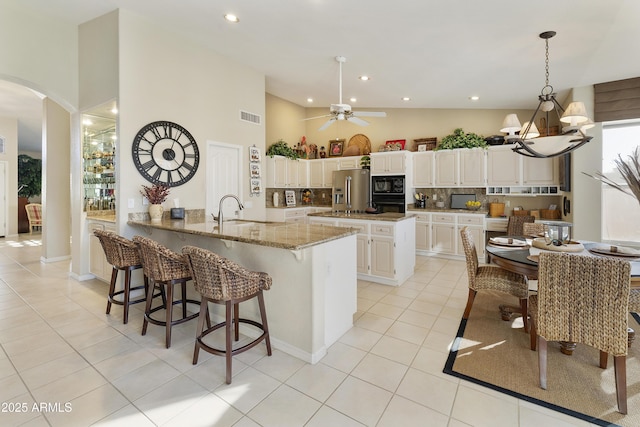 kitchen with black appliances, light stone counters, sink, white cabinetry, and decorative light fixtures