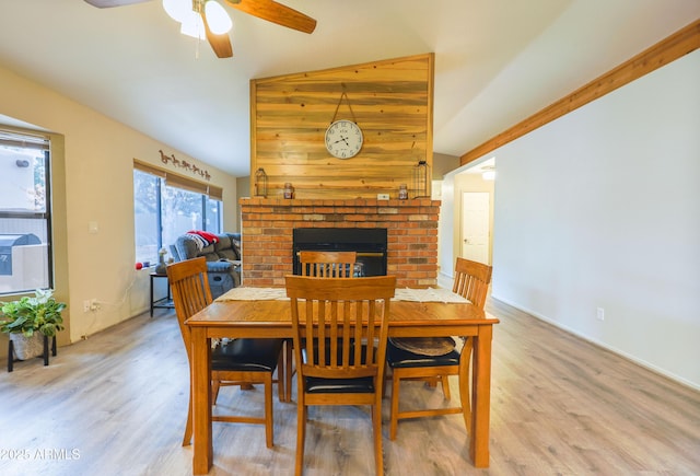 dining room with a fireplace, lofted ceiling, ceiling fan, and light wood-type flooring