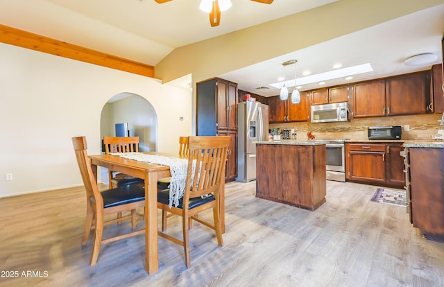 kitchen featuring appliances with stainless steel finishes, hanging light fixtures, decorative backsplash, a kitchen island, and lofted ceiling