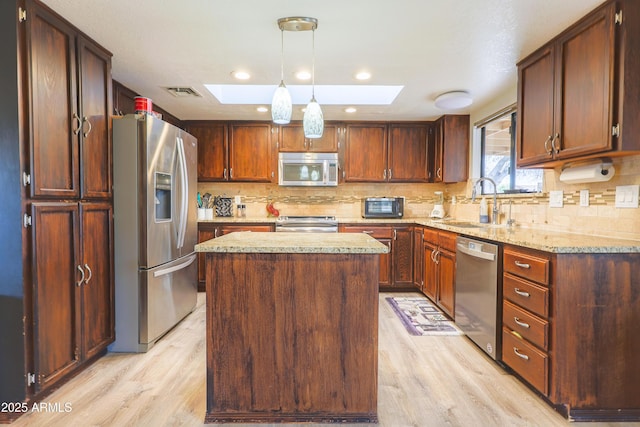 kitchen with light wood-type flooring, a skylight, a kitchen island, and appliances with stainless steel finishes