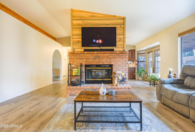 living room with light hardwood / wood-style flooring, vaulted ceiling, and a brick fireplace