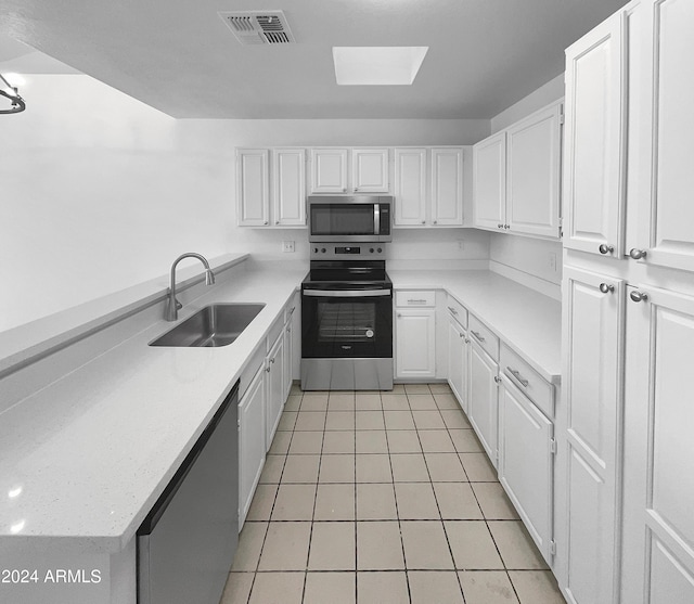 kitchen with appliances with stainless steel finishes, a skylight, sink, white cabinets, and light tile patterned flooring