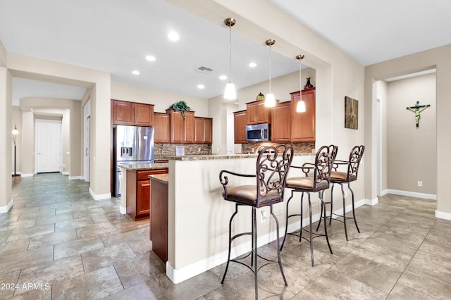 kitchen with pendant lighting, a kitchen breakfast bar, tasteful backsplash, light stone counters, and stainless steel appliances