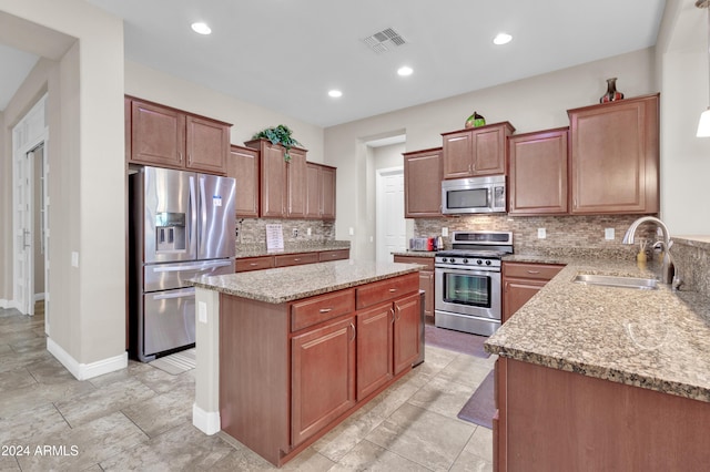 kitchen featuring sink, decorative backsplash, light stone countertops, appliances with stainless steel finishes, and a kitchen island