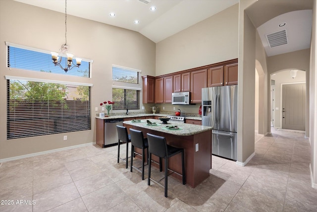 kitchen with appliances with stainless steel finishes, high vaulted ceiling, a breakfast bar area, hanging light fixtures, and a center island