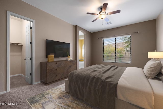 carpeted bedroom featuring a walk in closet and ceiling fan