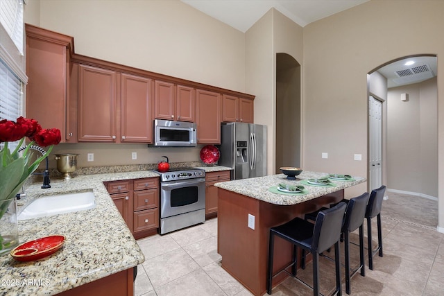 kitchen featuring a towering ceiling, sink, a center island, light stone counters, and stainless steel appliances