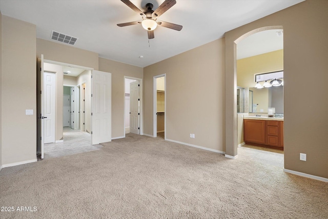 unfurnished bedroom with ensuite bathroom, a walk in closet, light carpet, and ceiling fan