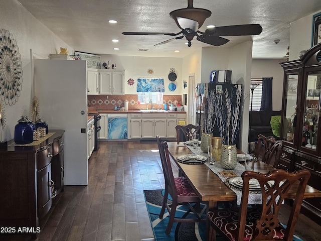 dining area with sink, a textured ceiling, ceiling fan, and dark wood-type flooring