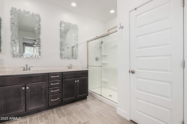 bathroom featuring a sink, wood tiled floor, a stall shower, and double vanity