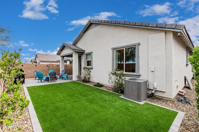 rear view of house featuring fence, central air condition unit, stucco siding, a lawn, and a patio