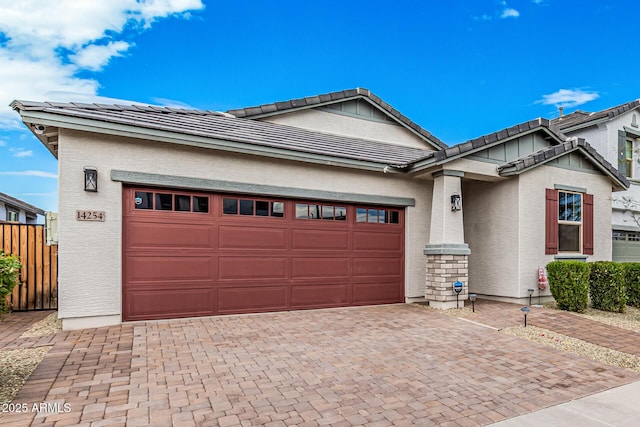 view of front of property featuring fence, stucco siding, a garage, a tiled roof, and decorative driveway