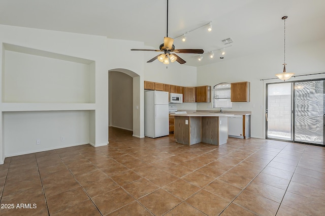 kitchen featuring a center island, white appliances, ceiling fan, arched walkways, and light countertops