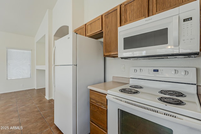 kitchen featuring brown cabinets, white appliances, tile patterned floors, and light countertops