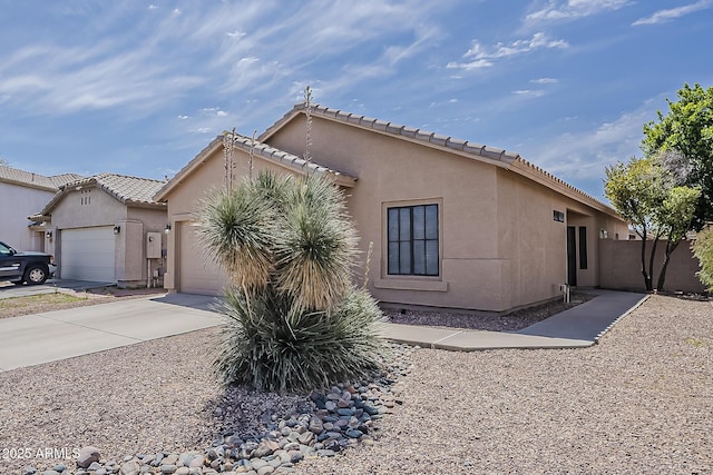 exterior space featuring a garage, stucco siding, a tile roof, fence, and driveway
