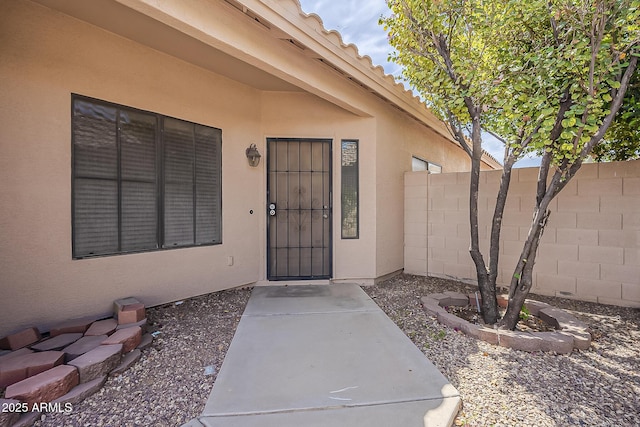 view of exterior entry featuring stucco siding and fence